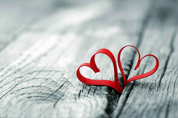 Red ribbon in heart shape at wooden background